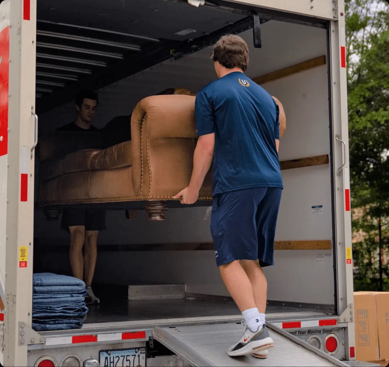 Undergrads college movers in Charlotte NC loading a leather armchair into a U-Haul truck with furniture pads and boxes